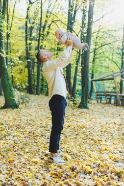 Mutlu genç baba, sıcak bir bahar ya da yaz gününde parkta oğluna sarılıyor. Parkta gün ışığı. Baba oğul doğada aile kavramı.