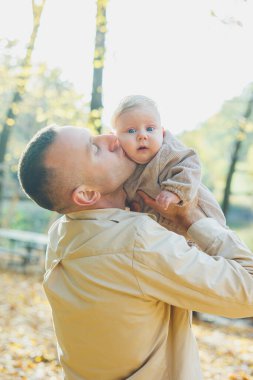 Mutlu genç baba, sıcak bir bahar ya da yaz gününde parkta oğluna sarılıyor. Parkta gün ışığı. Baba oğul doğada aile kavramı.