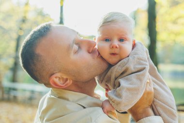 Mutlu genç baba, sıcak bir bahar ya da yaz gününde parkta oğluna sarılıyor. Parkta gün ışığı. Baba oğul doğada aile kavramı.