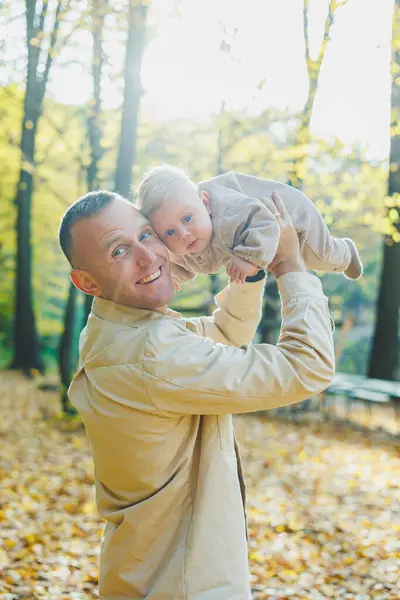 Happy young dad hug his little son in the sun on a warm spring or summer day in the park. Sunshine light in the park. Father and son family concept in nature