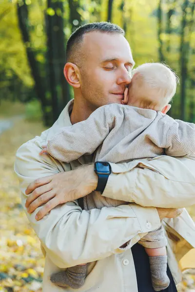Happy young dad hug his little son in the sun on a warm spring or summer day in the park. Sunshine light in the park. Father and son family concept in nature