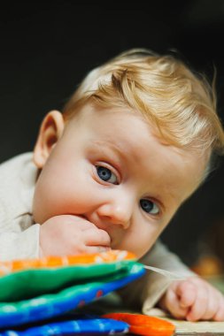 Çocuk karnının üzerinde sürünüyor. 6 aylık küçük bir bebek halıda sürünüyor ve gülümsüyor. Bir çocuk yerde bir oyuncakla oynuyor..