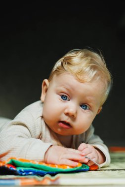 Çocuk karnının üzerinde sürünüyor. 6 aylık küçük bir bebek halıda sürünüyor ve gülümsüyor. Bir çocuk yerde bir oyuncakla oynuyor..