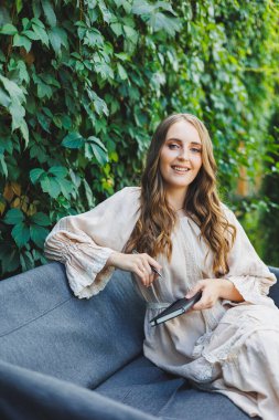 Elbiseli hoş bir genç kadın elinde bir defterle oturur ve bir yaz kafesinin terasına notlar alır. Gündelik şık yaz kıyafetleri içinde bir kadın.