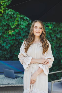 Yazlık bir kafede terasta elbise giymiş genç bir kadın. Gündelik şık yaz kıyafetleri içinde bir kadın.