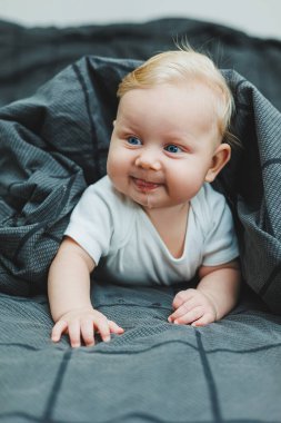 Beyaz elbiseli dört aylık küçük bir çocuk yatakta uzanıyor ve gülümsüyor. Gülümseyen bir bebek