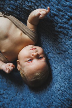 İki aylık bir bebek gri bir battaniyenin üzerinde örülmüş pantolonla yatıyor. Bebekler için kıyafetler.
