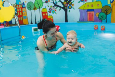 6 aylık bir bebek havuzda koçla yüzmeyi öğreniyor. Bebekler için yüzme havuzu. Çocuk gelişimi