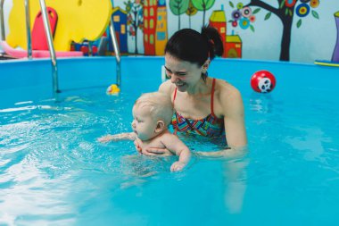6 aylık bir bebek havuzda koçla yüzmeyi öğreniyor. Bebekler için yüzme havuzu. Çocuk gelişimi