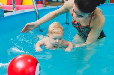 6 aylık bir bebek havuzda koçla yüzmeyi öğreniyor. Bebekler için yüzme havuzu. Çocuk gelişimi