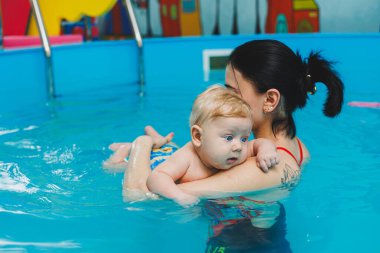 6 aylık bir bebek havuzda koçla yüzmeyi öğreniyor. Bebekler için yüzme havuzu. Çocuk gelişimi