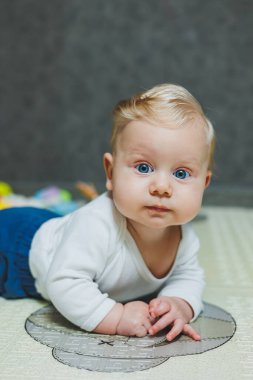 5 aylık bir bebek gülümsüyor ve gelişim paspasının üzerinde yatıyor. Çocuğun kişisel gelişimi.