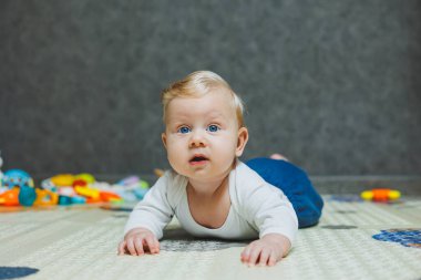 5 aylık bir bebek gülümsüyor ve gelişim paspasının üzerinde yatıyor. Çocuğun kişisel gelişimi.