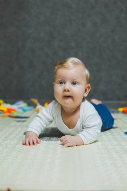 5 aylık bir bebek gülümsüyor ve gelişim paspasının üzerinde yatıyor. Çocuğun kişisel gelişimi.