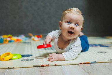 Beş aylık tatlı bir çocuk halıda yalan söylüyor ve oynuyor. Çocuk yerde yatıyor. Küçük şirin bir bebek emeklemeyi öğreniyor..