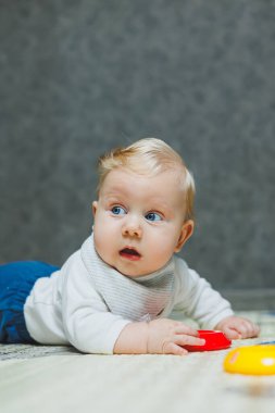 Dört aylık bir çocuk halıya uzanıyor ve oyuncaklarla oynuyor. Çocuk başını tutuyor. Bir bebek yerde sürünmeyi öğrenir.