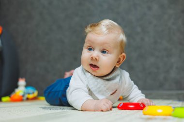 Dört aylık bir çocuk halıya uzanıyor ve oyuncaklarla oynuyor. Çocuk başını tutuyor. Bir bebek yerde sürünmeyi öğrenir.