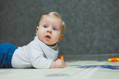 Dört aylık bir çocuk halıya uzanıyor ve oyuncaklarla oynuyor. Çocuk başını tutuyor. Bir bebek yerde sürünmeyi öğrenir.