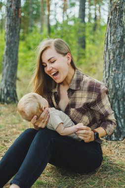 Sevimli bir anne çimenlerin üzerinde kollarında küçük bir çocukla oturuyor. Doğada küçük bir çocukla yürüyüş..