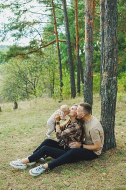 Genç bir aile doğada kucağında küçük bir oğlanla oturuyor. Kollarında bir bebekle yürüyen bir aile..