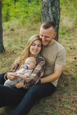 Genç bir aile doğada kucağında küçük bir oğlanla oturuyor. Kollarında bir bebekle yürüyen bir aile..