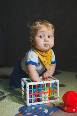 6 aylık küçük bir çocuk gelişim minderinin üzerinde oturuyor ve taşaklı bir sınıflandırıcıyla oynuyor. Bebekler için eğitici oyunlar. Çocuklarda el hareketliliğinin gelişimi