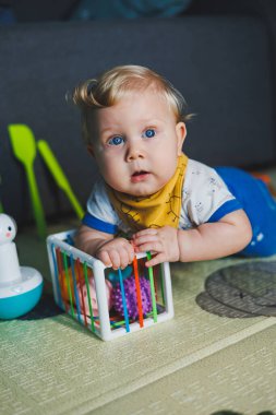 Çocuk paspasın üzerinde yatıyor, yumuşak toplarla oynuyor. Bebeğin el becerileri için eğitici oyuncaklar. Çocuk gelişimi. Duyusal deneyim