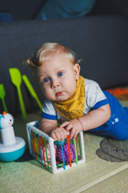 6 aylık küçük bir çocuk gelişim minderinin üzerinde oturuyor ve taşaklı bir sınıflandırıcıyla oynuyor. Bebekler için eğitici oyunlar. Çocuklarda el hareketliliğinin gelişimi