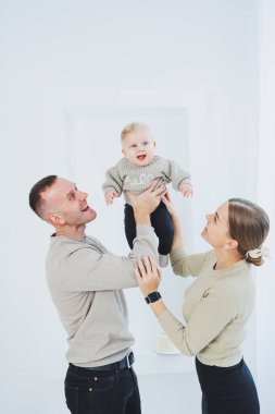 Gülümseyen anne ve baba kucağında bir çocuk. Anne, baba ve kollarındaki gülümseyen bebek beyaz arka planda izole edilmiş. Mutlu genç aile.