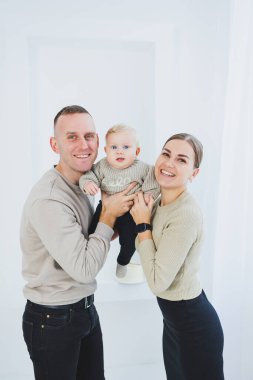 Gülümseyen anne ve baba kucağında bir çocuk. Anne, baba ve kollarındaki gülümseyen bebek beyaz arka planda izole edilmiş. Mutlu genç aile.