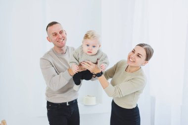 Gülümseyen anne ve baba kucağında bir çocuk. Anne, baba ve kollarındaki gülümseyen bebek beyaz arka planda izole edilmiş. Mutlu genç aile.