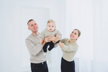 Gülümseyen anne ve baba kucağında bir çocuk. Anne, baba ve kollarındaki gülümseyen bebek beyaz arka planda izole edilmiş. Mutlu genç aile.