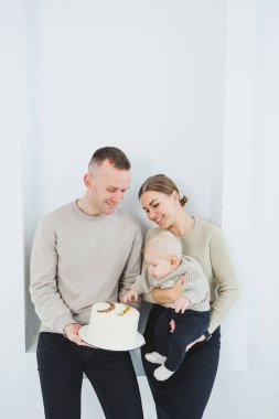 Gülümseyen anne ve baba bir çocuk ve bir tatil pastası tutuyor. Anne, baba ve kollarındaki gülümseyen bebek beyaz arka planda izole edilmiş. Mutlu genç aile.
