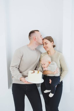 Gülümseyen anne ve baba bir çocuk ve bir tatil pastası tutuyor. Anne, baba ve kollarındaki gülümseyen bebek beyaz arka planda izole edilmiş. Mutlu genç aile.