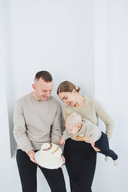 Gülümseyen anne ve baba bir çocuk ve bir tatil pastası tutuyor. Anne, baba ve kollarındaki gülümseyen bebek beyaz arka planda izole edilmiş. Mutlu genç aile.