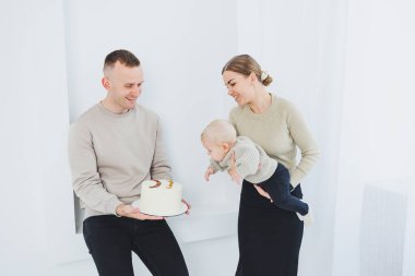 Gülümseyen anne ve baba bir çocuk ve bir tatil pastası tutuyor. Anne, baba ve kollarındaki gülümseyen bebek beyaz arka planda izole edilmiş. Mutlu genç aile.
