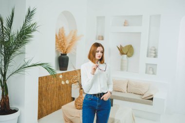 Açık alanda gözlüklü hoş bir kadın, iş yerinde çalışan, rahatlayan, uzaktan çalışan, beyaz tişört ve kot pantolon giyen.