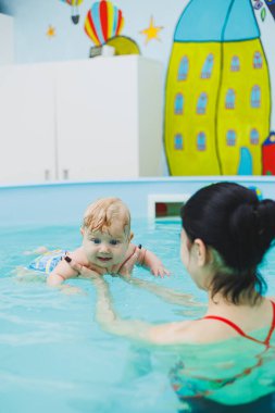 Antrenör bebeğe yüzme, çocuklar için yüzme havuzu öğretiyor. Çocuk gelişimi.