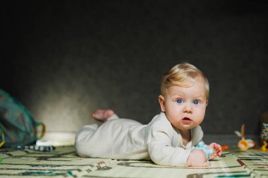 7 aylık bir bebek halının üzerinde uzanıyor ve oynuyor. Çocuk başını tutuyor. Bir bebek yerde sürünmeyi öğrenir. Bej tulumlu bir çocuk..
