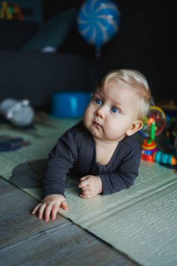 7 aylık bir bebek halıda sürünüyor. Çocuk başını tutuyor. Bir bebek yerde sürünmeyi öğrenir. Gri şortlu bir çocuk..