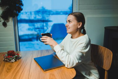 Masada otururken dizüstü bilgisayarda çalışan gülümseyen mutlu kadın. Evde klavyede çalışan ve daktilo yazan yaratıcı genç bir kadın. Ev konseptinde çalış