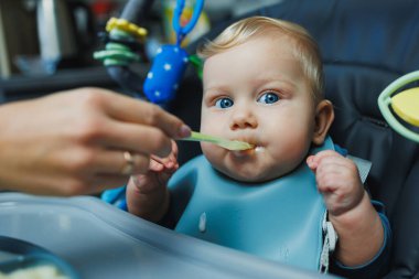 Bebeğin ilk beslenmesi tamamlayıcı püre yemektir. Kaşıkla bebek maması. Bir anne 6 aylık oğlunu püre ile besler. Ebeveynler bebeklerini yatakta yiyecekle besler.
