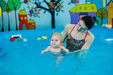 9 aylık küçük bir çocuk bir koçla havuzda yüzmeyi öğreniyor..