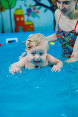 9 aylık küçük bir çocuk bir koçla havuzda yüzmeyi öğreniyor..