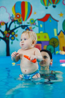 7 aylık bir çocuk bir koçla havuzda yüzmeyi öğreniyor. Çocuklar için yüzme dersleri. Çocuk gelişimi