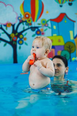 7 aylık bir çocuk bir koçla havuzda yüzmeyi öğreniyor. Çocuklar için yüzme dersleri. Çocuk gelişimi