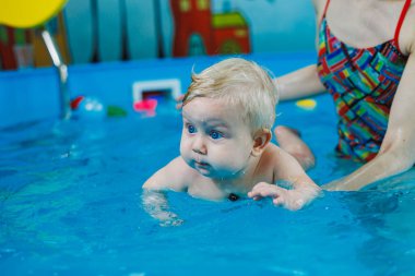 9 aylık küçük bir çocuk bir koçla havuzda yüzmeyi öğreniyor..