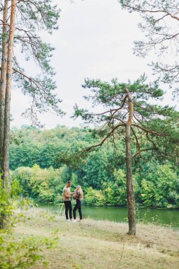 Parkta bir bebekle anne ve babanın yürüyüşü. Kollarında küçük bir bebek olan mutlu bir aile çifti doğanın içinde duruyor. Küçük bir çocukla aile tatili.
