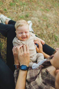 Annesinin kollarında, 2 aylık bir çocuğun yakın plan fotoğrafı var. Bebek annesinin kollarında yatarken gülümsüyor..