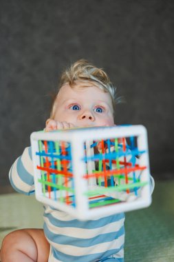 7 aylık küçük bir çocuk dik oturmayı öğreniyor. Bir bebek yerde otururken oyuncaklarla oynar. Bebekler için eğitici oyuncaklar.